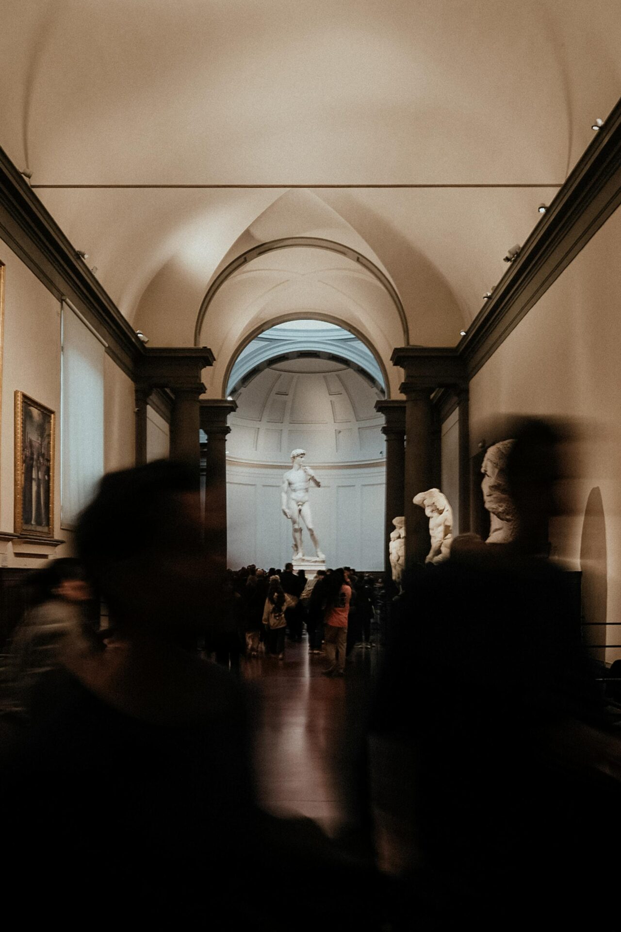 Visitors inside Accademia Gallery observing a statue,