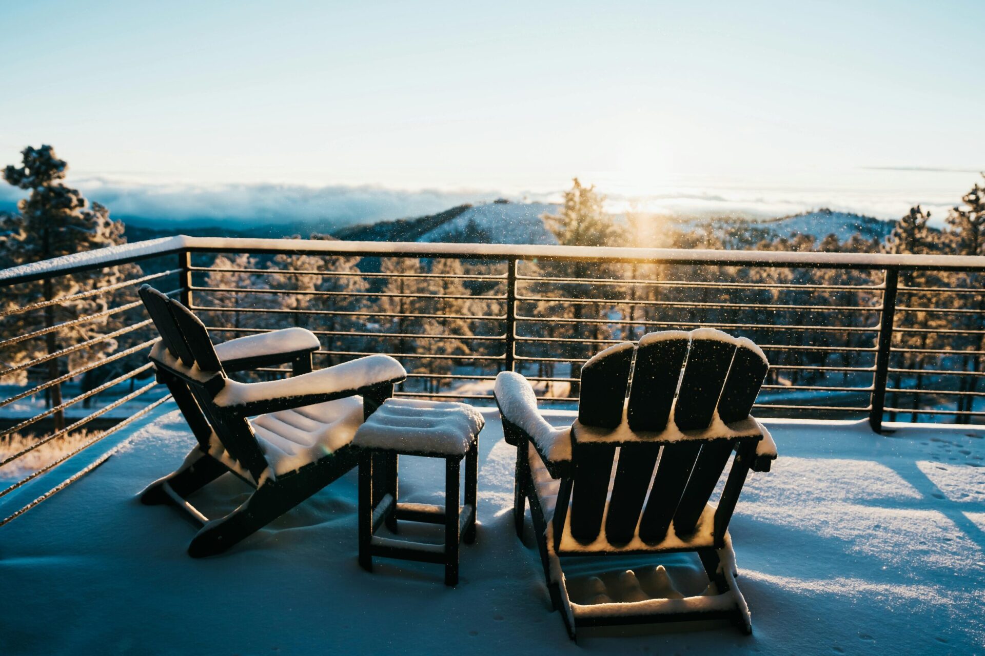 A balcony with two chairs covered with snow. A view of mountain peaks during winter.