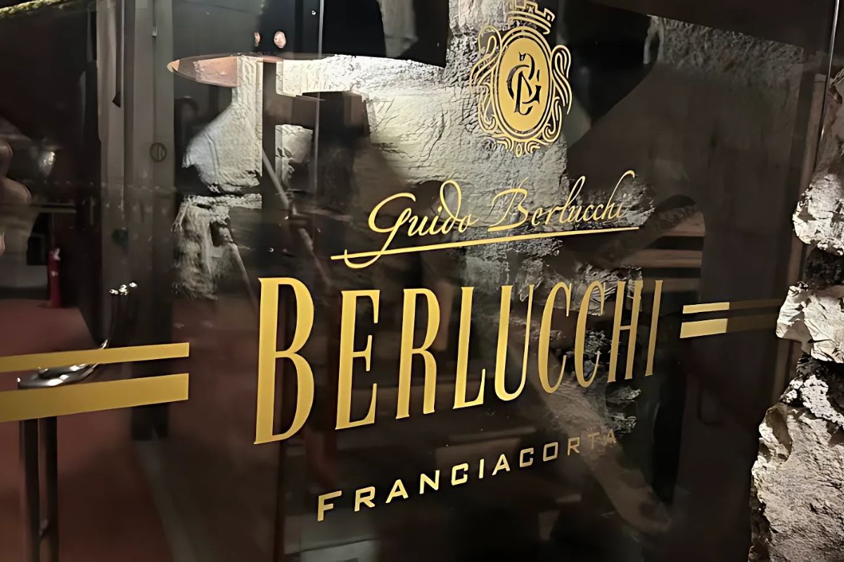 A glass door displays the "Berlucchi" logo in gold lettering, with "Guido Berlucchi" in script above and "Franciacorta" below. The background shows a textured, possibly stone or cellar-like interior
