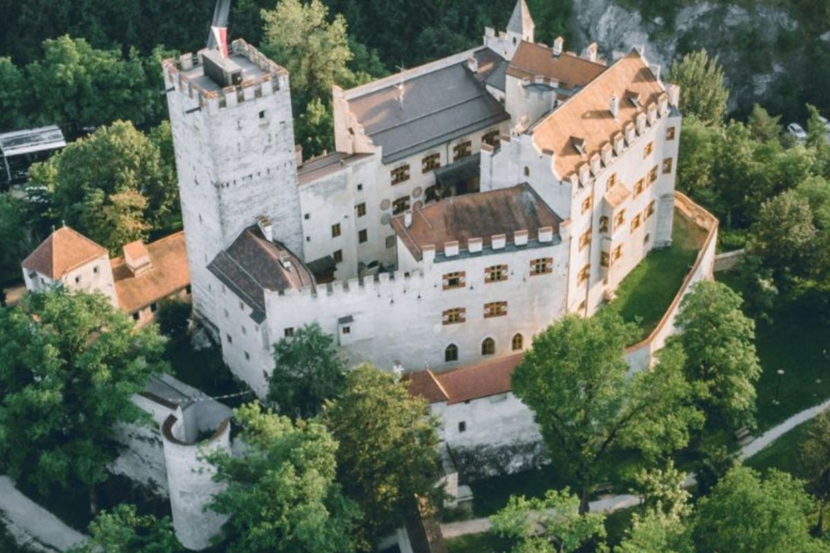 Close-up aerial view of Brunico Castle, a medieval fortress perched on a hill in Brunico, Italy, surrounded by lush greenery and part of the town below.