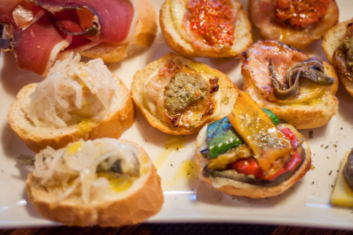 Assorted cicchetti, Venetian-style tapas, served on crusty bread with toppings like cured meats, seafood, roasted vegetables, and cheese.