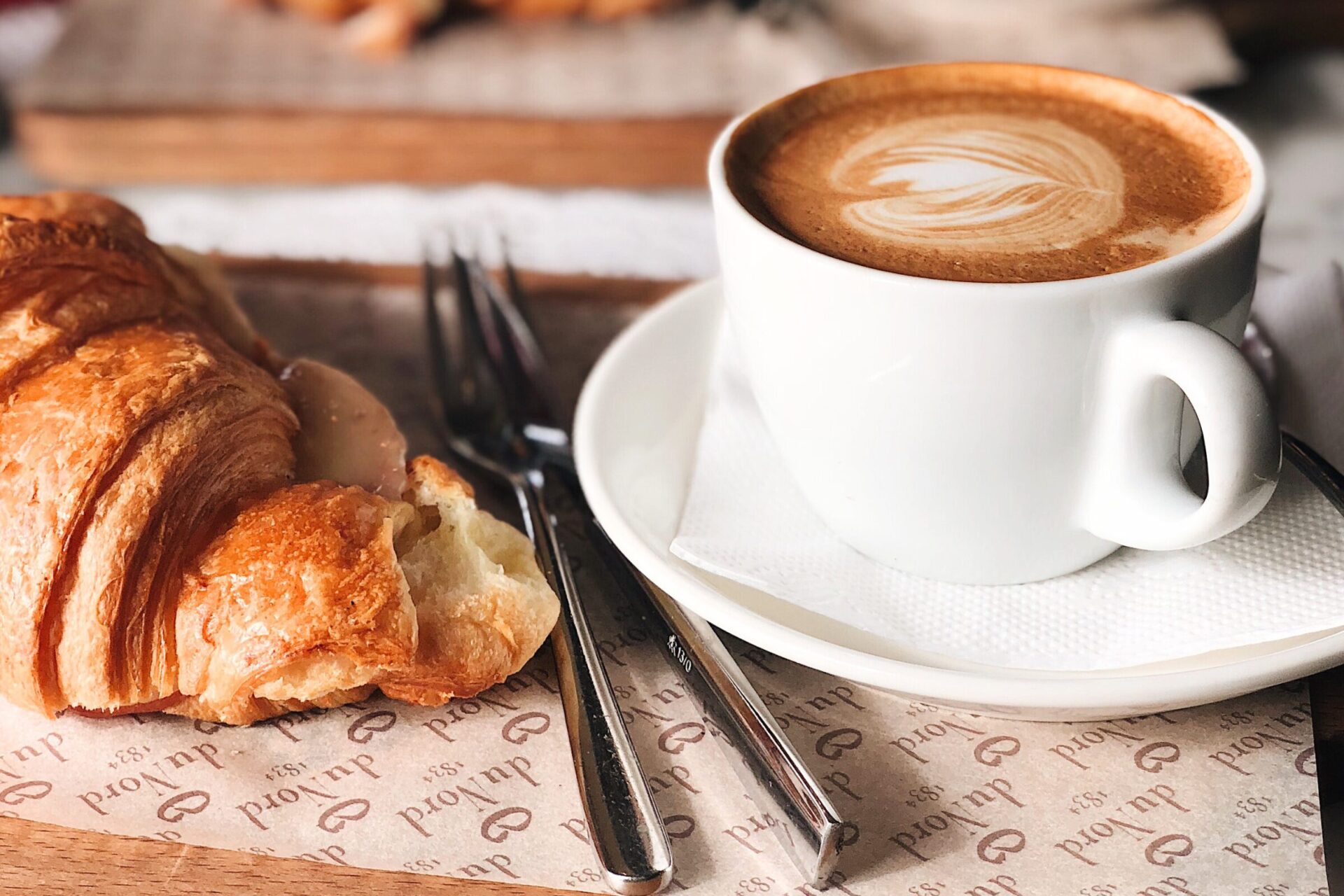 A cup of coffee with latte art and a piece of croissant - European breakfast