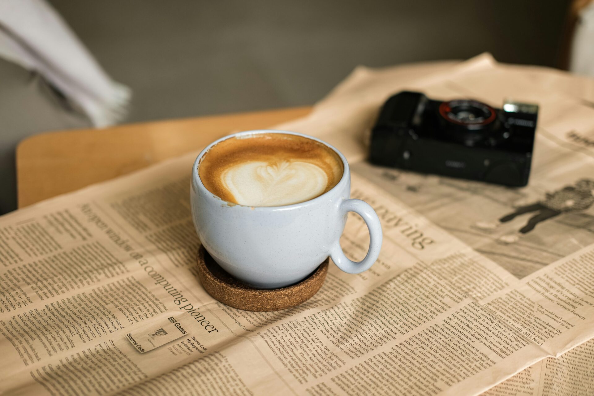 A cup of coffee or latte on a coffee table with a newspaper and a digital camera