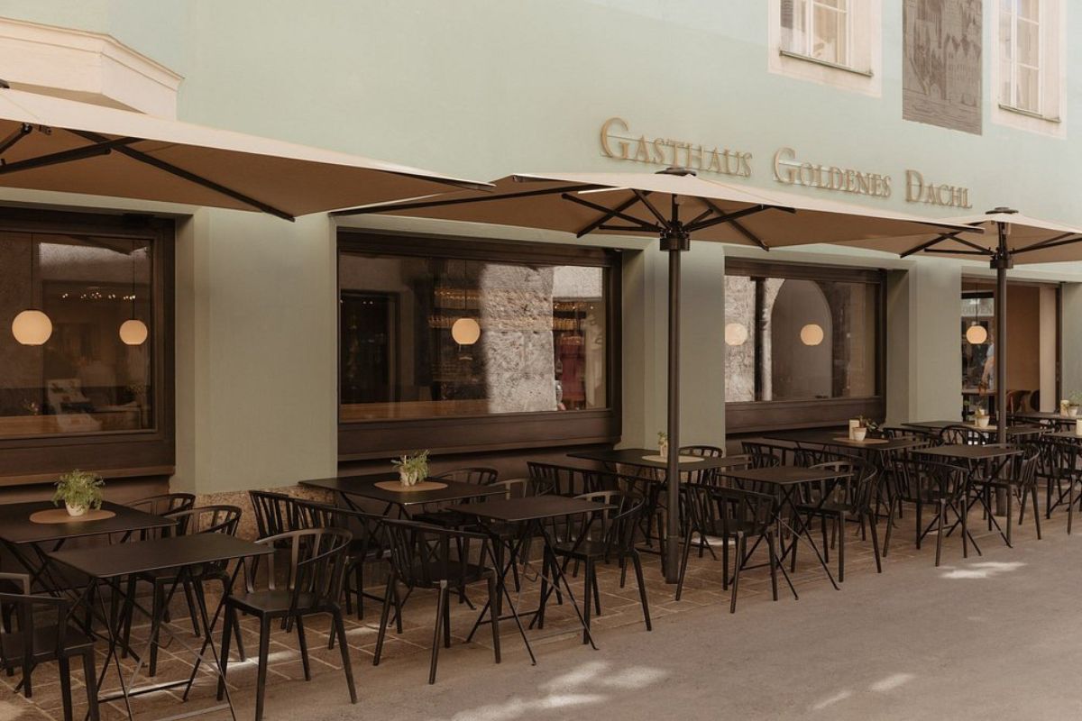 Outdoor seating area of the Gasthaus Goldenes Dachl restaurant with tables and chairs under umbrellas, with the restaurant's name displayed on the building.