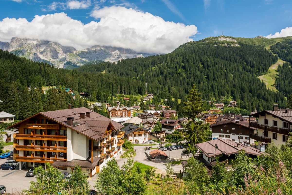 Scenic view of Hotel Crepes De Sela in Val Rendena, near Madonna di Campiglio, Italy, nestled amidst forested mountains and a village.