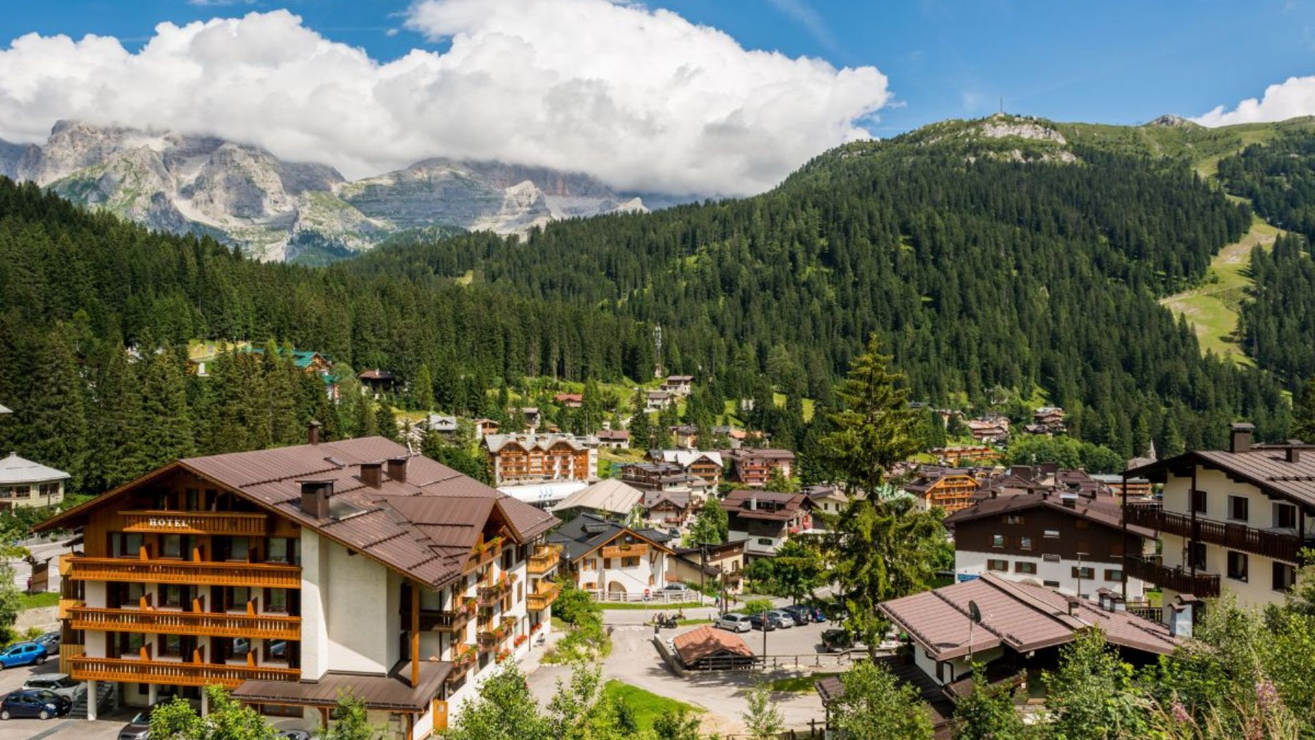 Scenic view of Hotel Crepes De Sela in Val Rendena, near Madonna di Campiglio, Italy, nestled amidst forested mountains and a village.