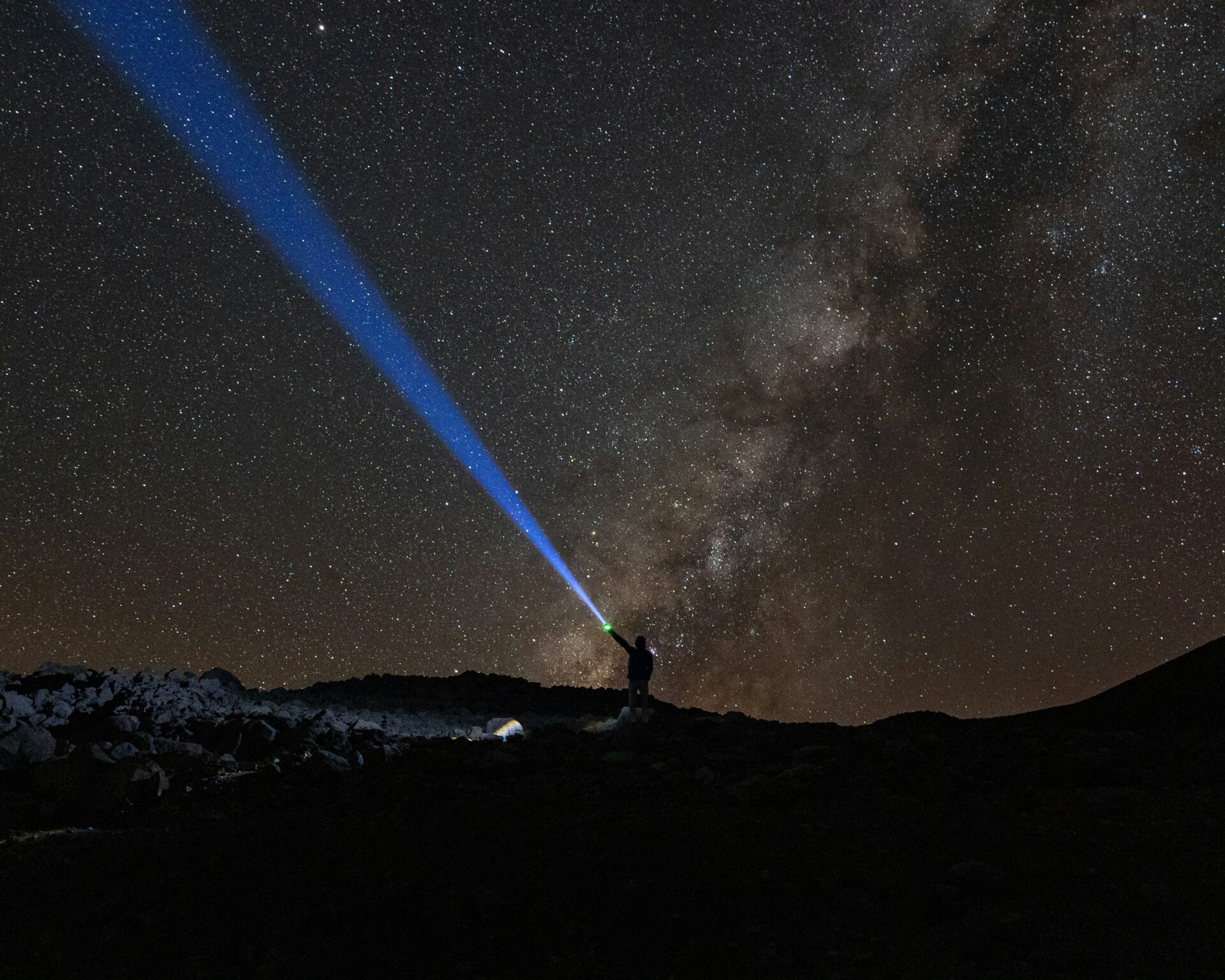 A man holding a flashlight under the stars at the Mauna Kea Observatories at night