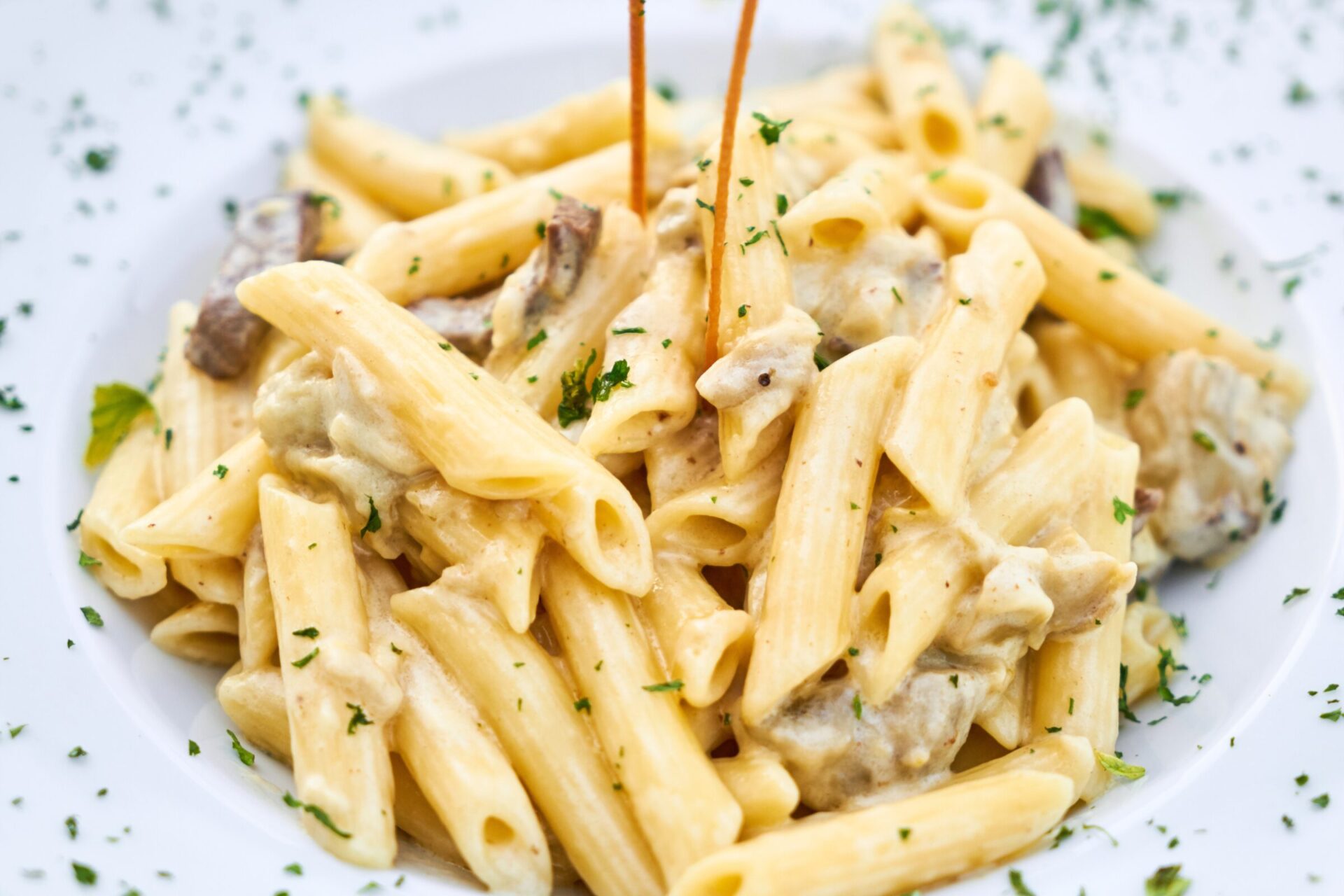 A plate of penne pasta - Italian pasta - with chicken or mushroom and green herbs.