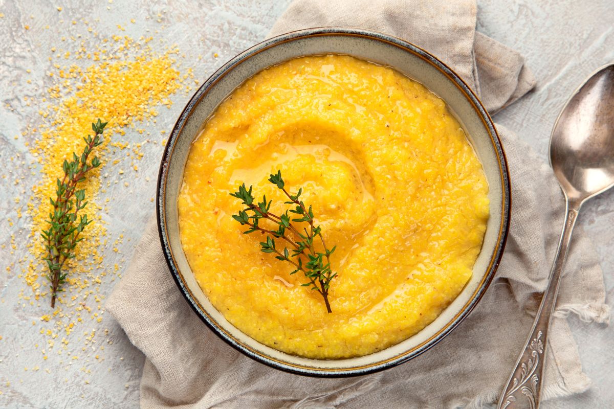 A warm, creamy bowl of traditional Italian polenta, drizzled with olive oil and garnished with fresh thyme, served on a rustic linen cloth with a vintage spoon.