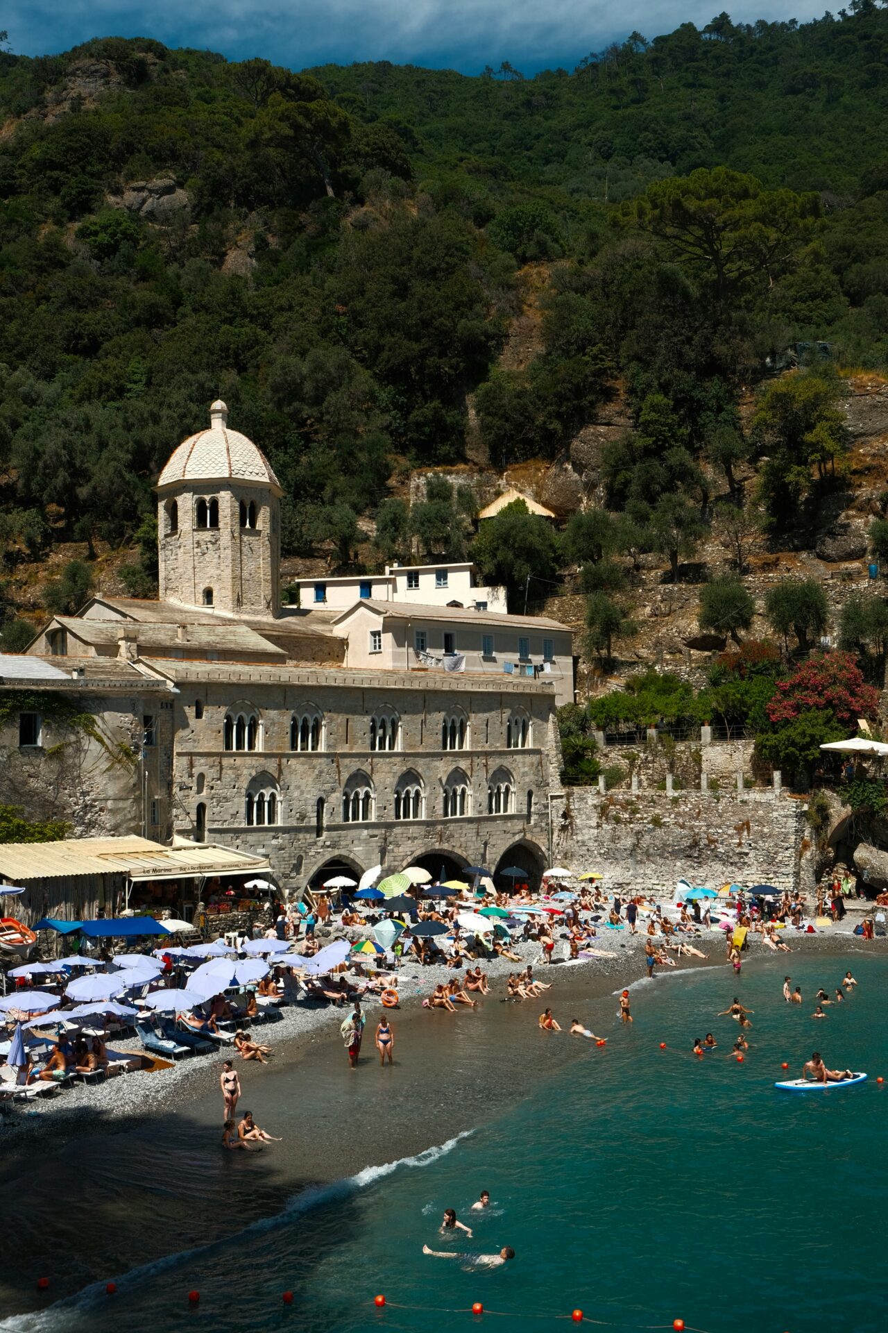 San Fruttuoso Abbey overlooking a vibrant scene with people swimming and relaxing in the crystal-clear turquoise waters