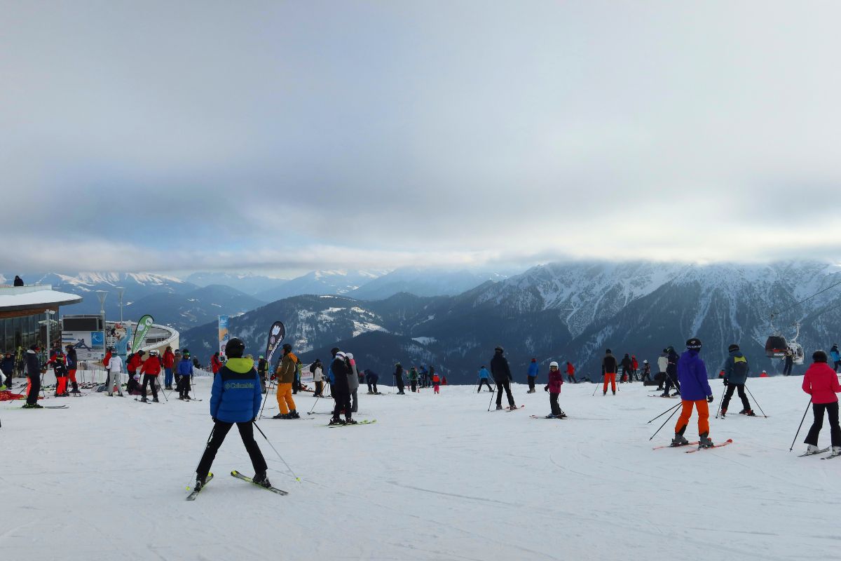 A group of skiers on the snowy slopes of Kronplatz Ski Resort, Plan de Corones, Brunico, Italy, with the Dolomite mountains visible in the background under a cloudy sky.