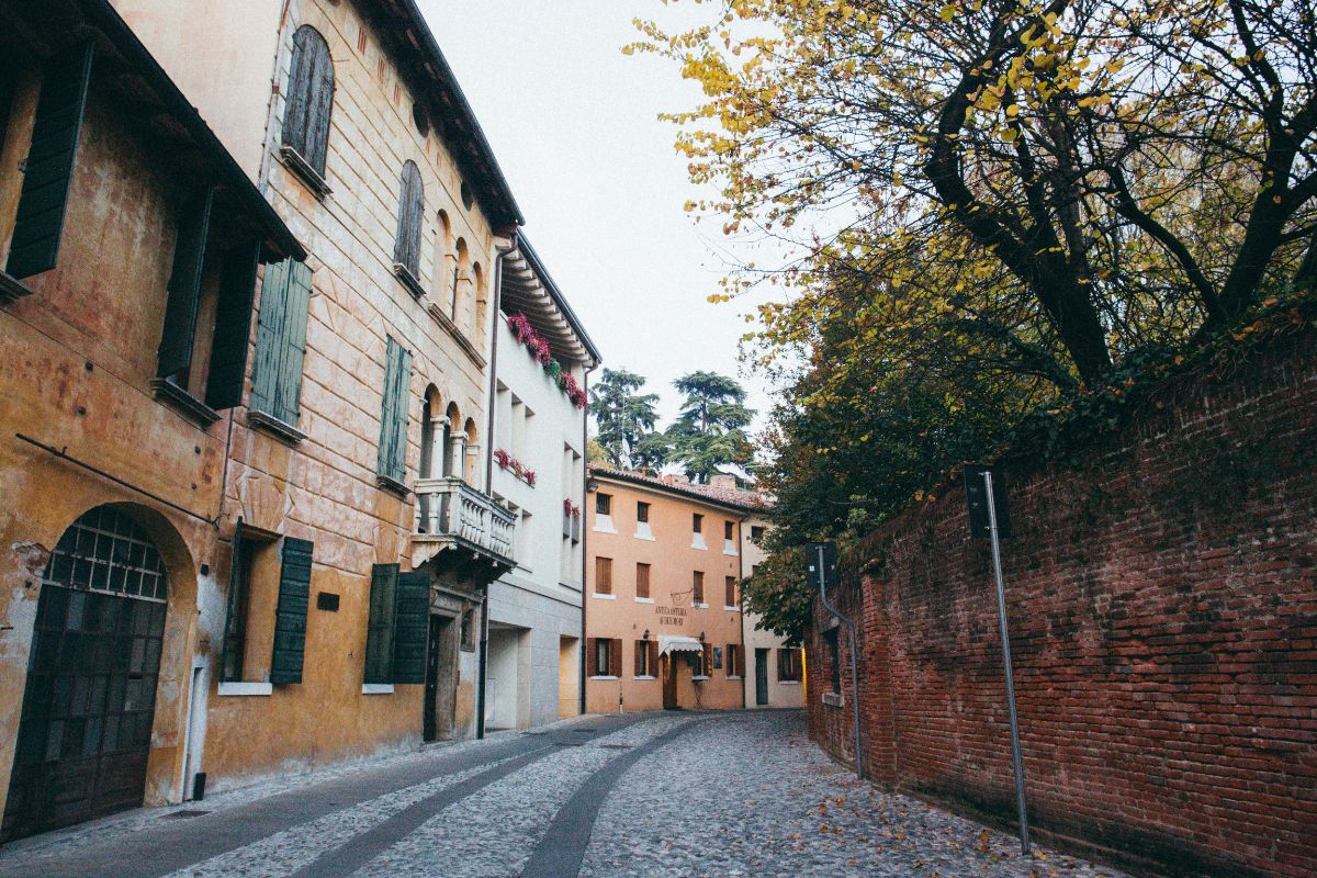 Cobblestone street in Veneto, Northern Italy, lined with historic buildings, green shutters, and autumn trees creating a peaceful, old-world atmosphere.