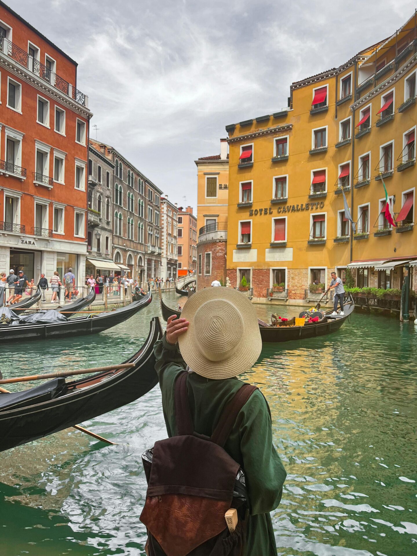 Traveler wearing a wide-brimmed hat and backpack admiring a scenic canal in Venice