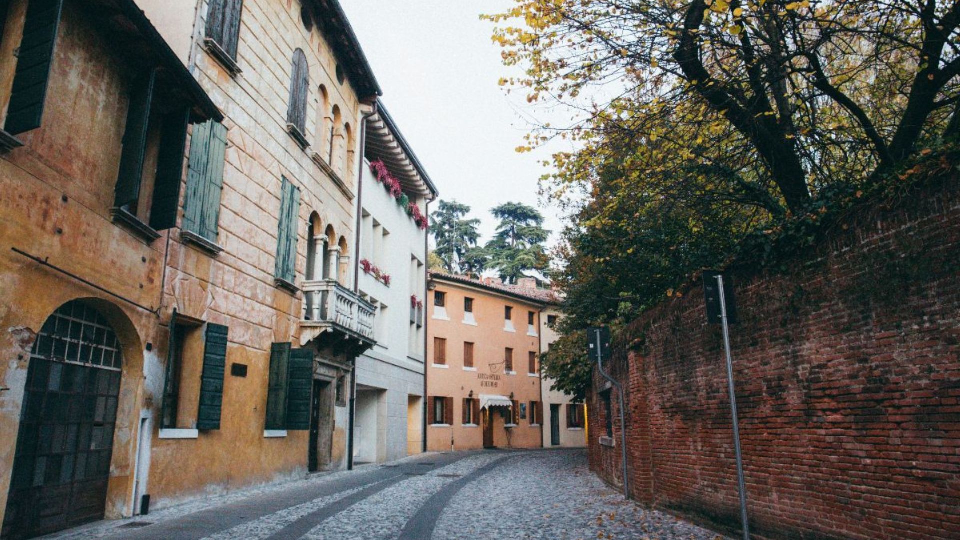 Cobblestone street in Veneto, Northern Italy, lined with historic buildings, green shutters, and autumn trees creating a peaceful, old-world atmosphere.