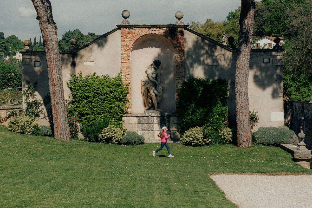 Garden of Villa Rotonda near Vicenza, Italy, featuring a classical statue set against an elegant stone wall, with a child running across the lush green lawn.