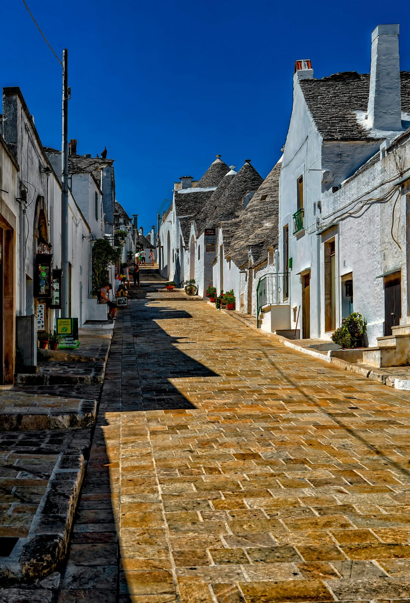 A peaceful, sunlit street in Alberobello with iconic trulli homes