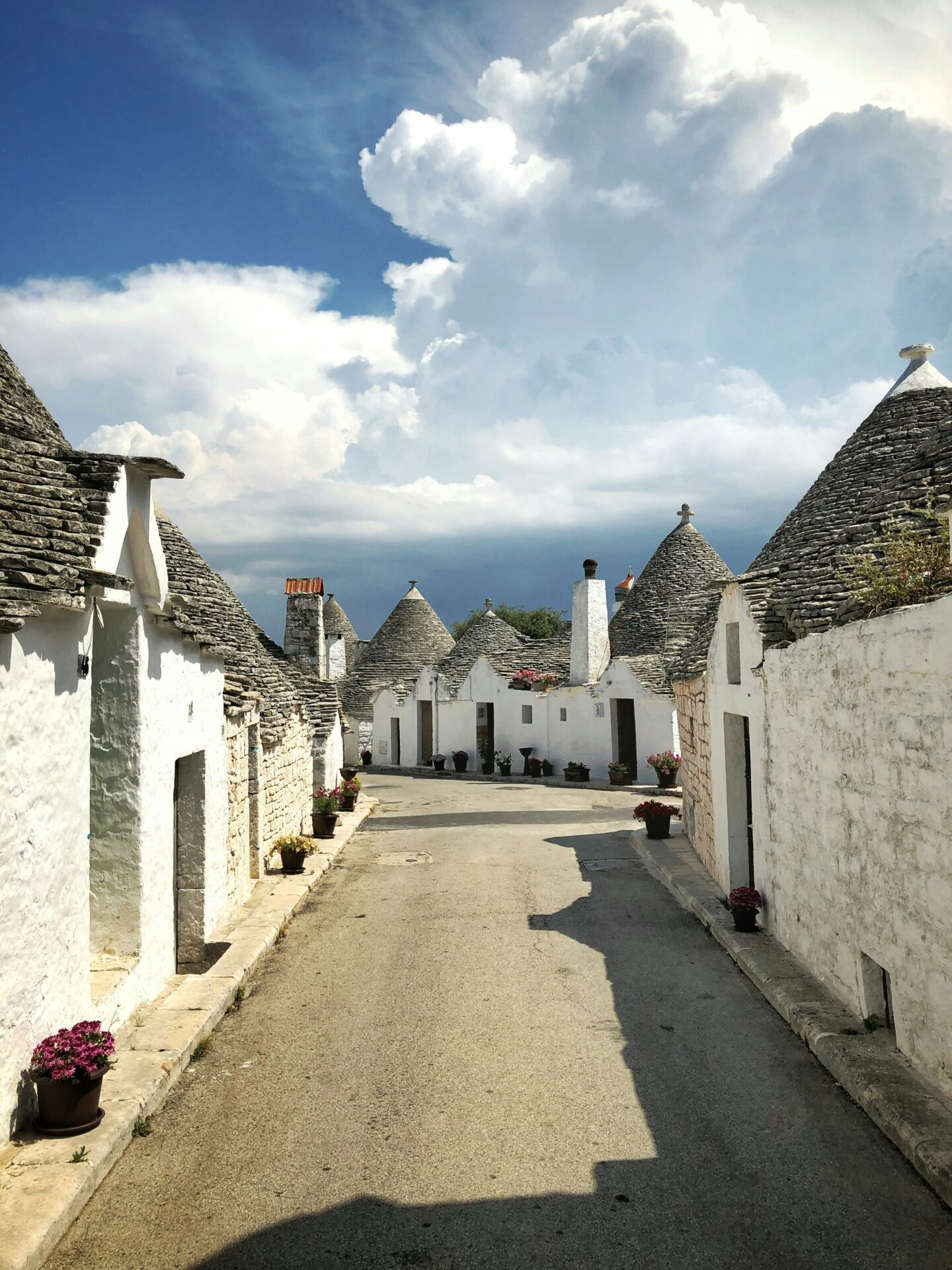 A narrow cobblestone street in Alberobello, Italy, lined with traditional whitewashed trulli houses