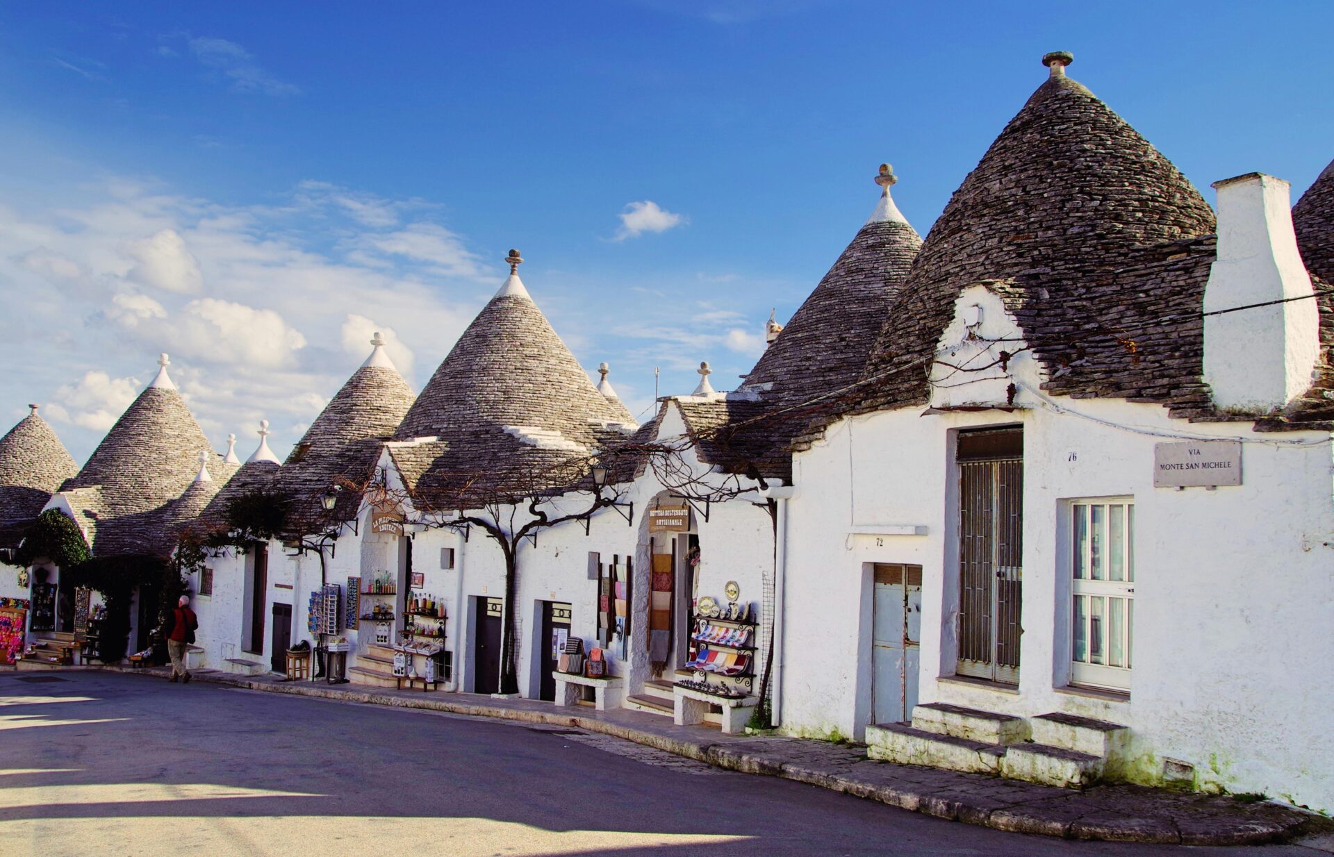 Traditional Trulli houses in Alberobello, Italy, with whitewashed stone walls and distinctive conical roofs under a blue sky.