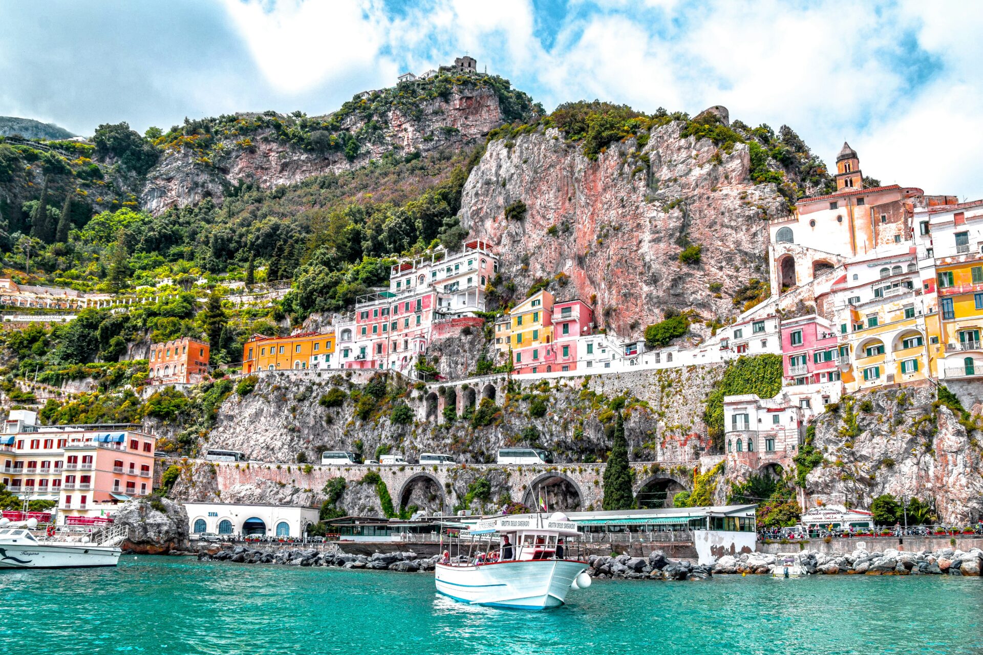 Colorful buildings perched on cliffs along the coastline of Amalfi, Italy, with a boat floating on the turquoise sea.