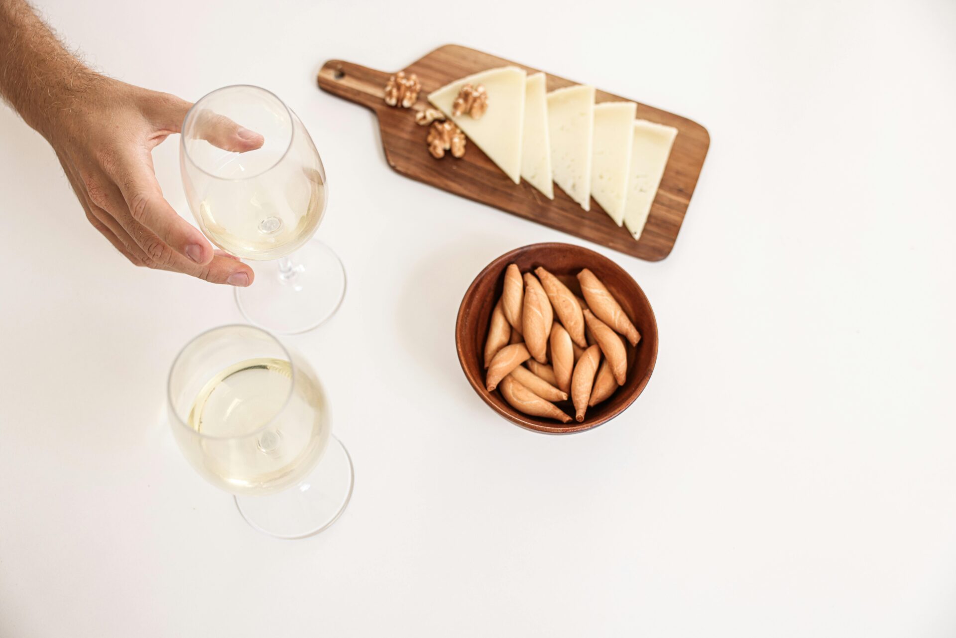 A Person Holding a Glass of Wine Near the Cheese on a Wooden Board.