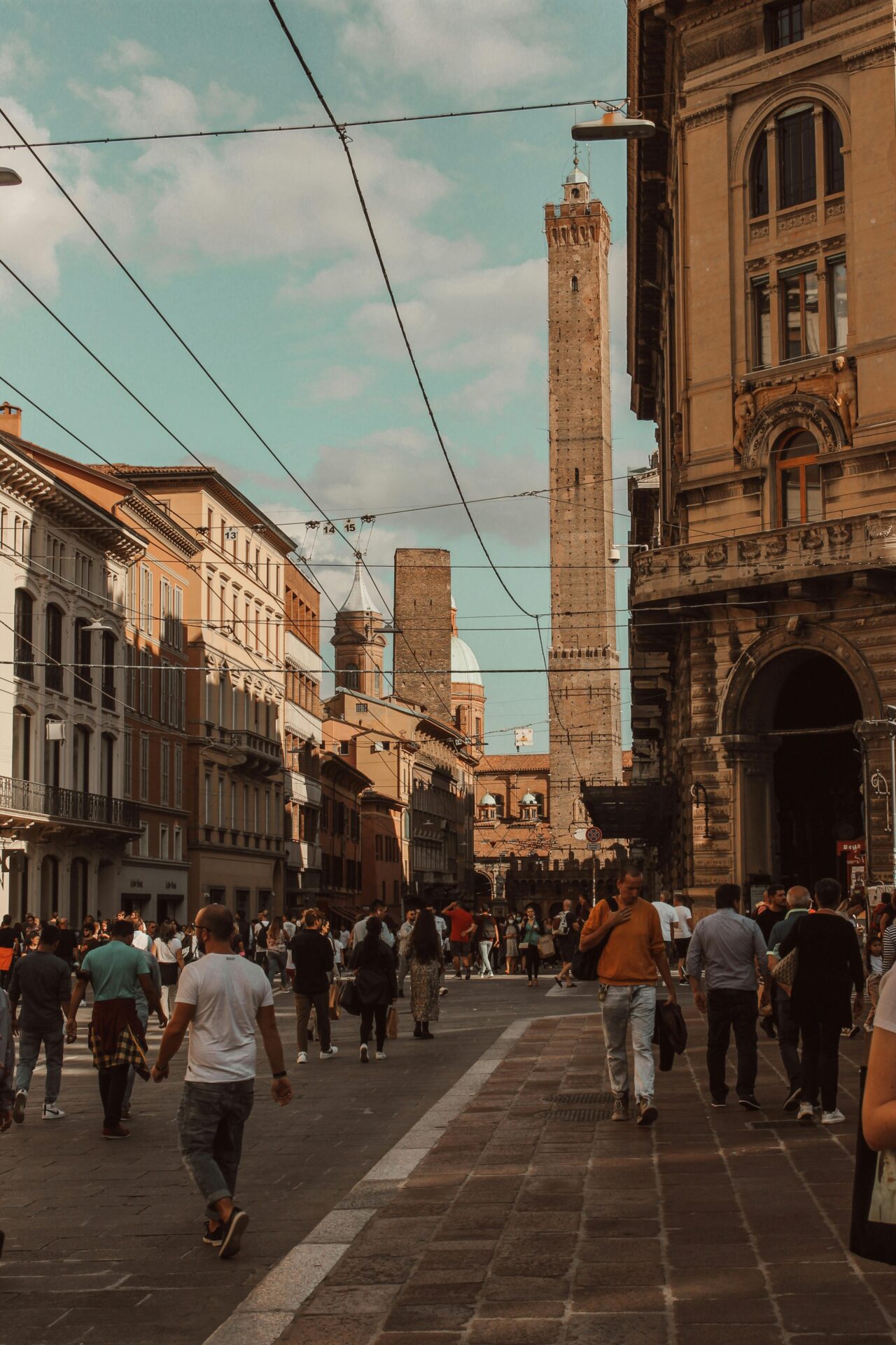The iconic Bologna Tower in Italy, with a bustling scene of people walking outside, capturing the vibrant atmosphere and historic charm of the city.