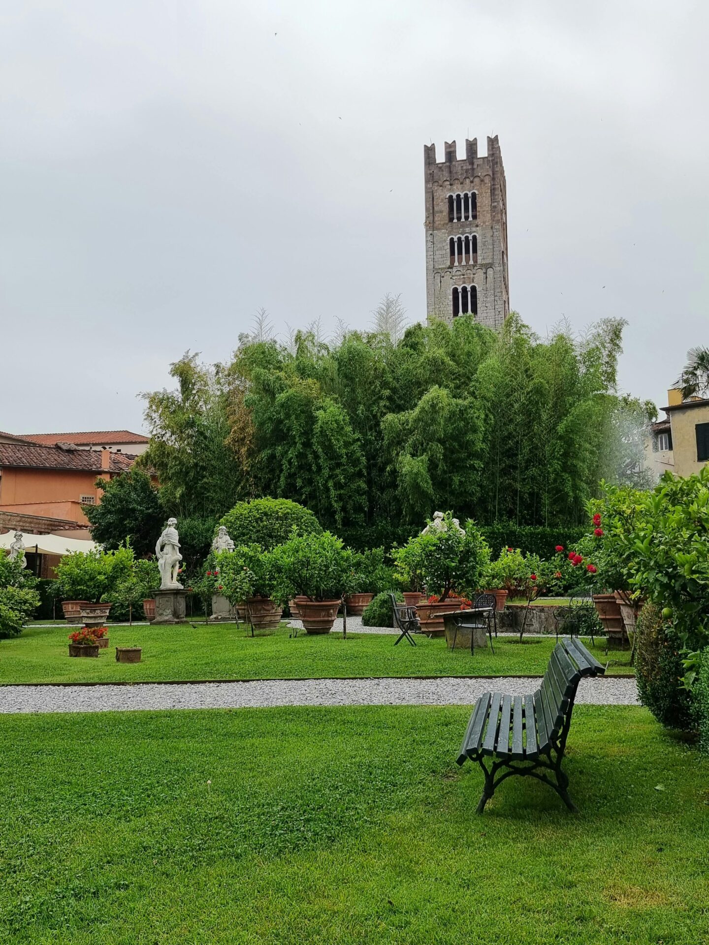 A serene view of the Botanical Garden of Lucca, Italy, with lush greenery, vibrant flowers, and well-maintained paths winding through trees and plants, surrounded by historic stone walls.