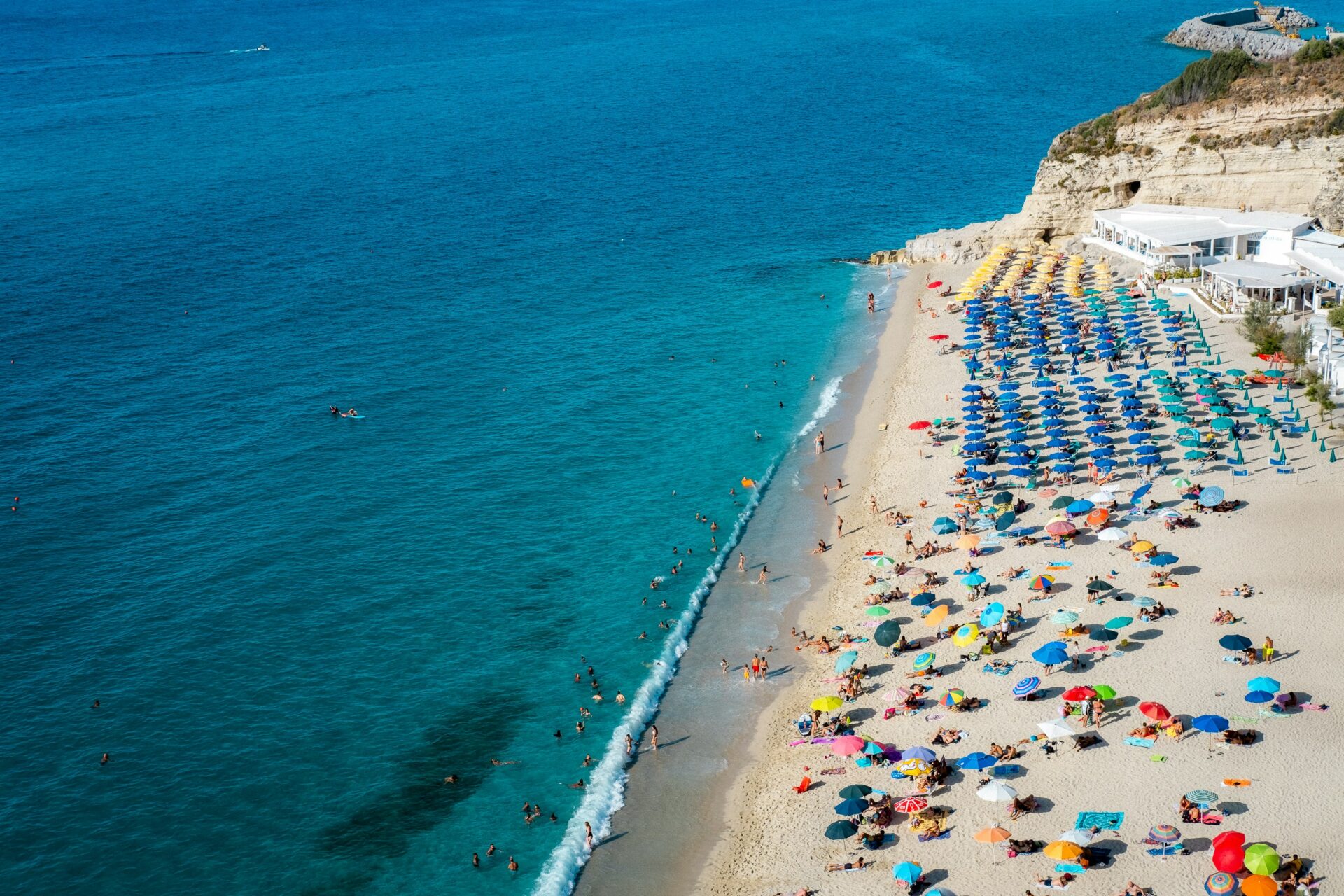 Busy Calabria beach with colorful umbrellas and people enjoying the sun by the sea