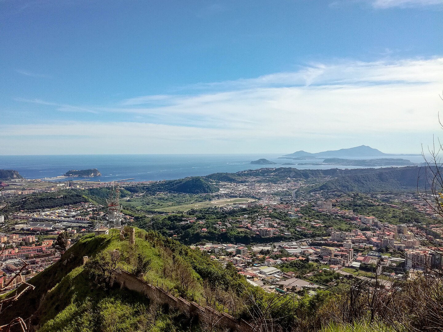 A dramatic volcanic landscape at Campi Flegrei, with steaming fumaroles, cracked earth, and rugged hills under a partly cloudy sky near Naples, Italy
