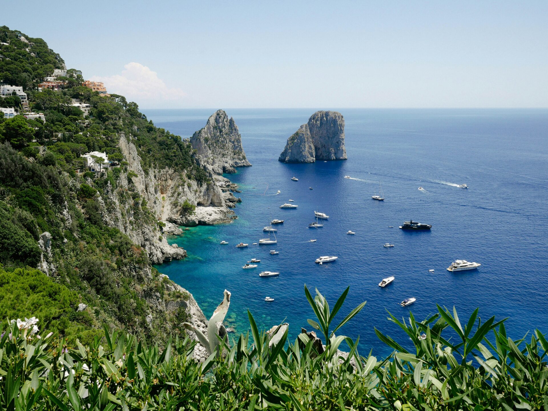 Scenic view of the rocky coastline and Faraglioni sea stacks in Capri, Italy, with boats scattered across the deep blue water.