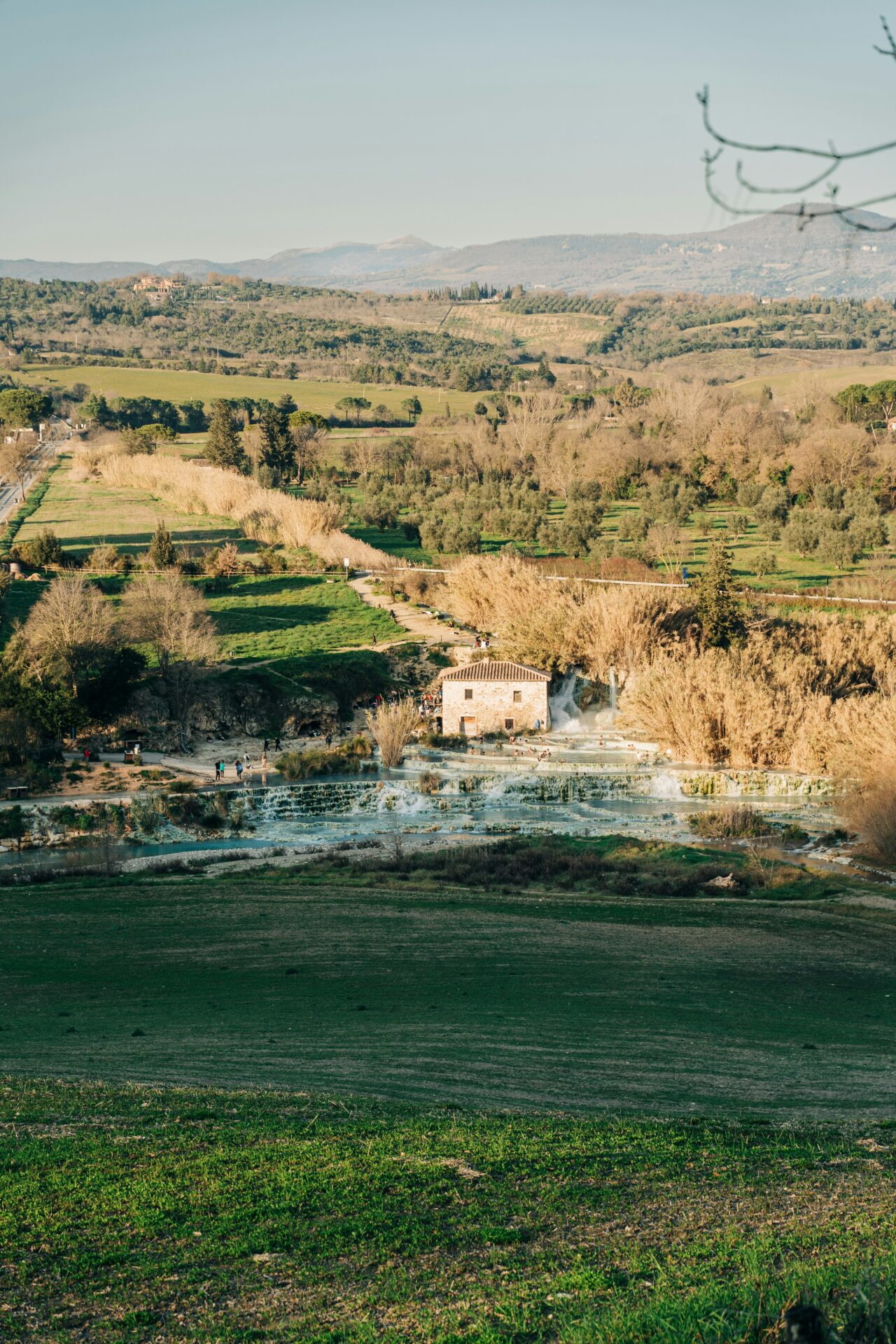 Cascate del Mulino, a natural thermal waterfall in Saturnia, Italy, with steaming turquoise water cascading over limestone terraces surrounded by lush greenery.
