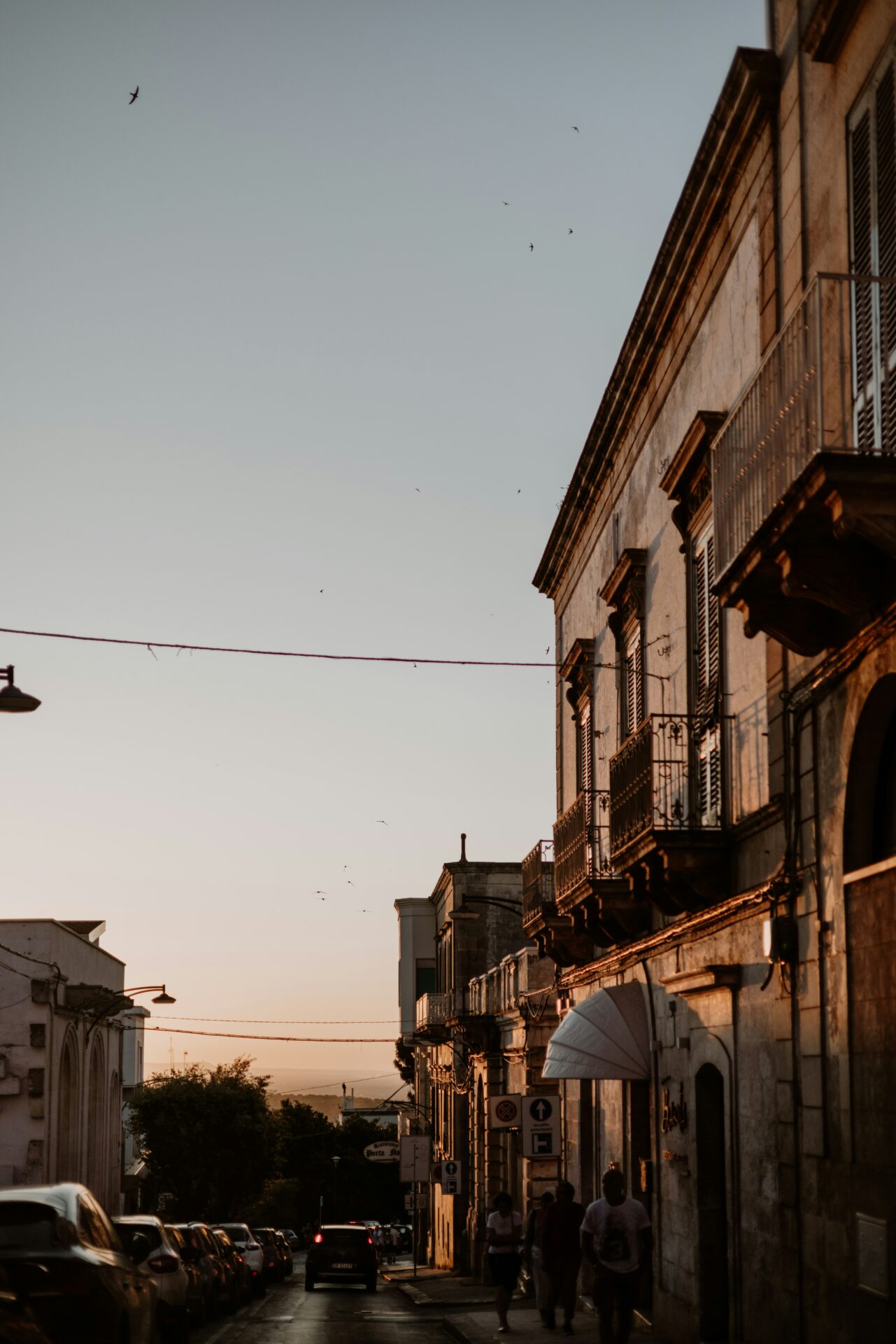 Charming view of a centro storico with narrow cobblestone streets, historic stone buildings, balconies with flowers, and warm sunlight casting soft shadows.