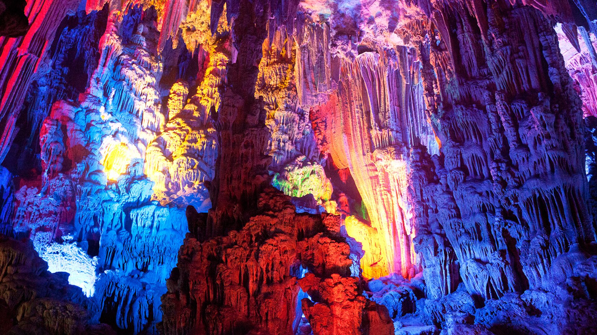 Image shows the colorful inside of China’s Reed Flute Cave.