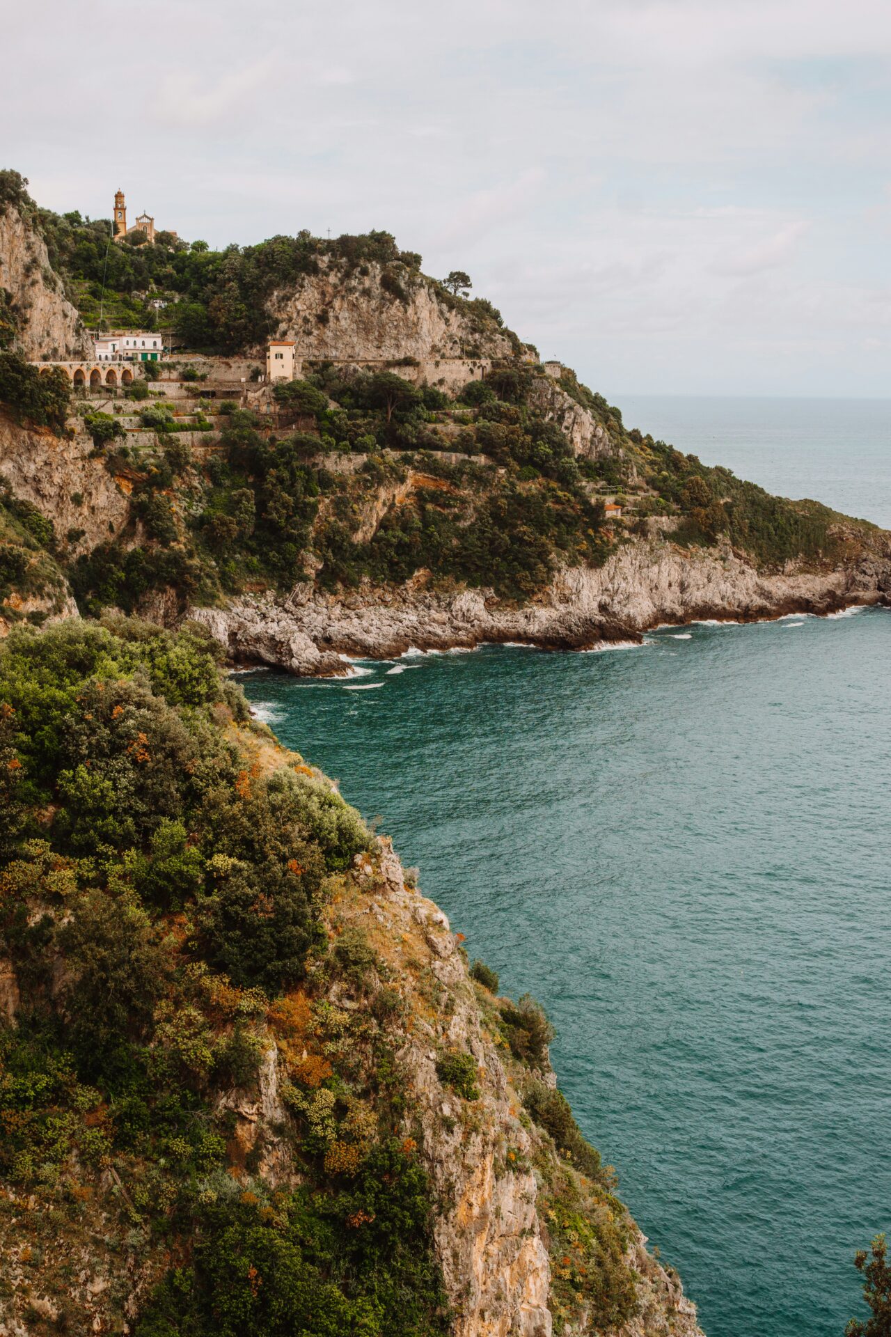Conca dei Marini, Italy cliff above the turquoise sea, surrounded by lush greenery and rocky coastline.