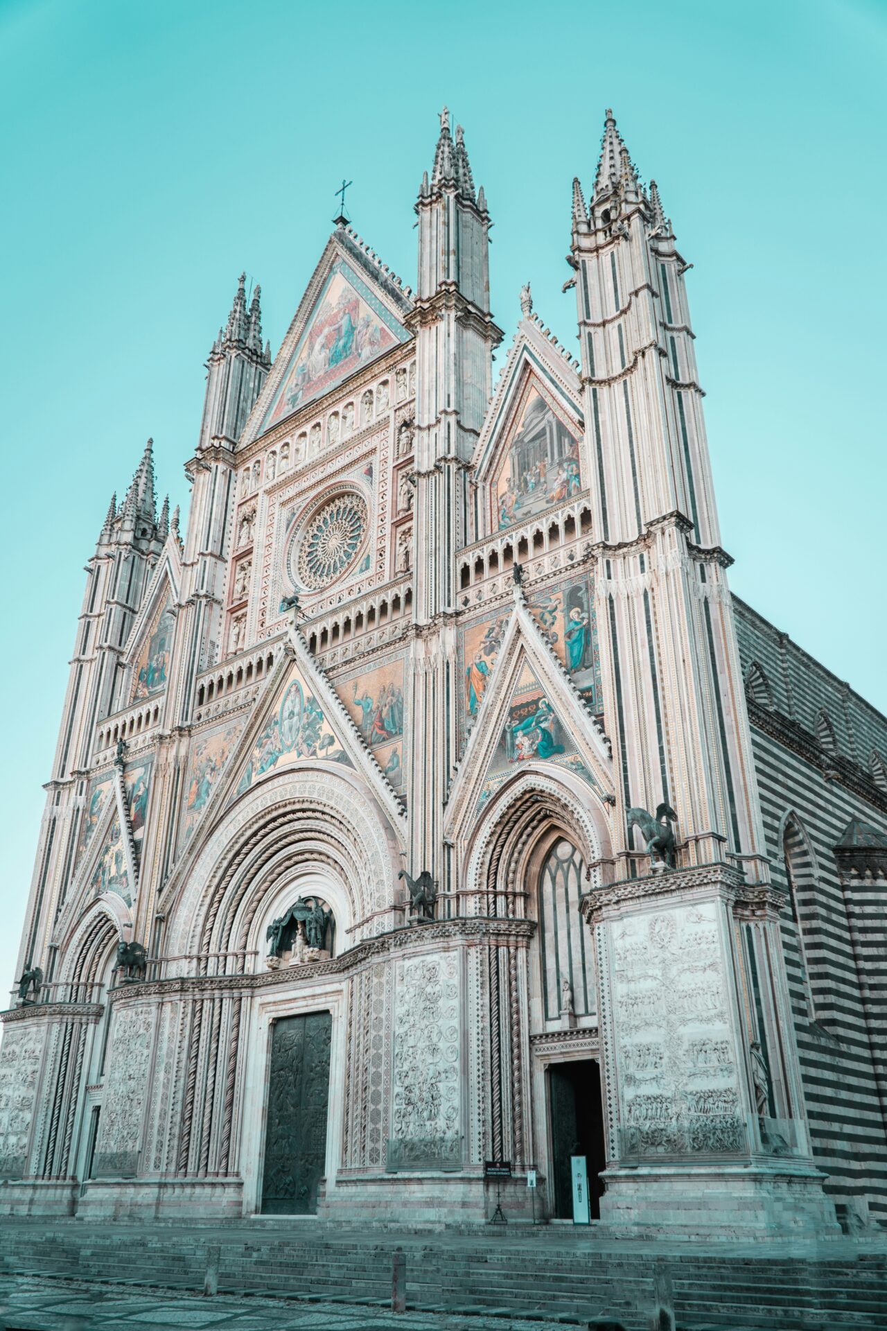 Magnificent façade of the Duomo di Orvieto, adorned with intricate mosaics, rose windows, and Gothic spires under a clear blue sky.