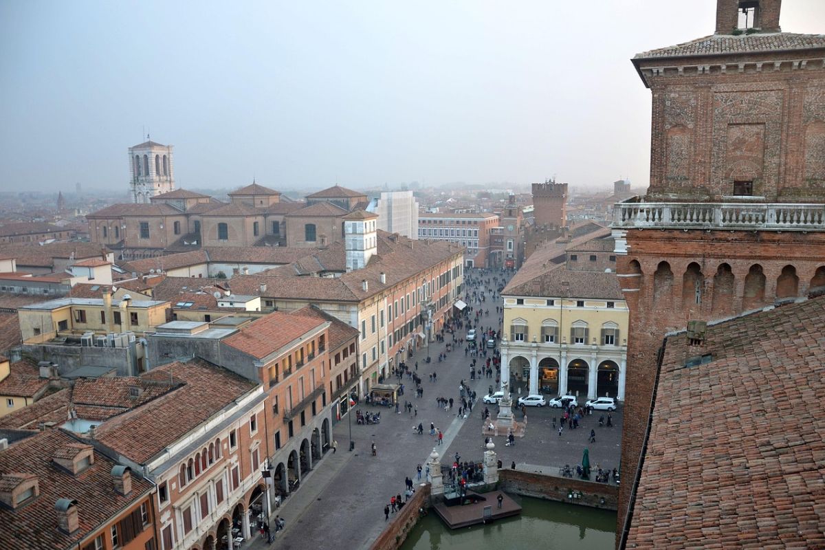 The image shows an aerial view of Ferrara, Italy, likely featuring the Ferrara Cathedral (also known as the Duomo di Ferrara) and the Castello Estense.