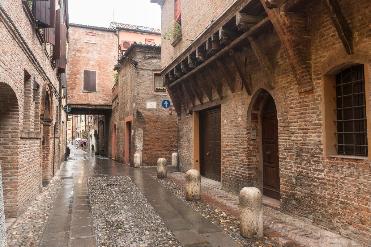 The image shows a street in Ferrara, Italy, specifically Via delle Volte, which is known for its medieval architecture.