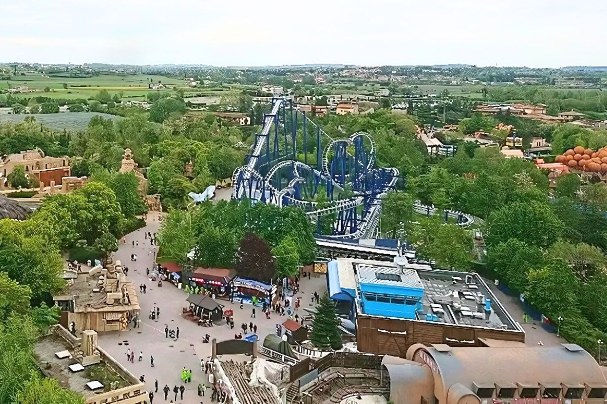 Aerial view of Gardaland amusement park featuring the Blue Tornado roller coaster amidst lush greenery and park attractions.
