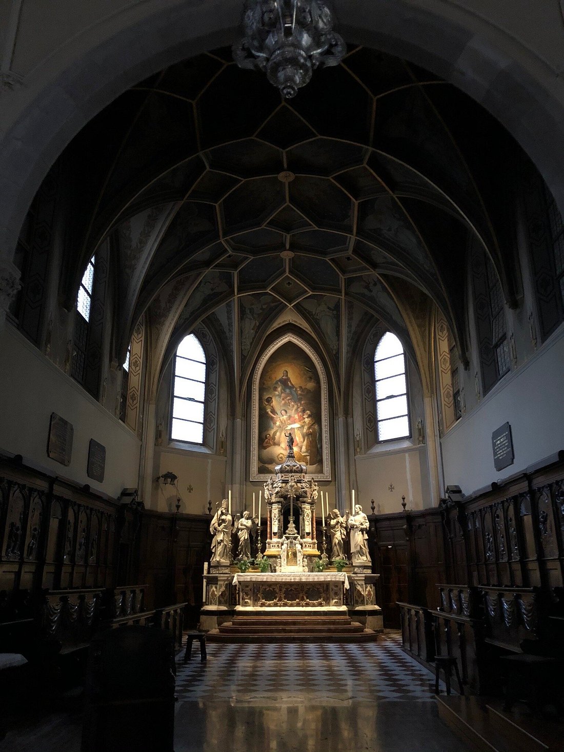 Interior of Gorizia Cathedral in Italy, featuring a beautifully decorated altar with statues, stained glass windows, a checkered floor, and a vaulted ceiling with intricate designs.