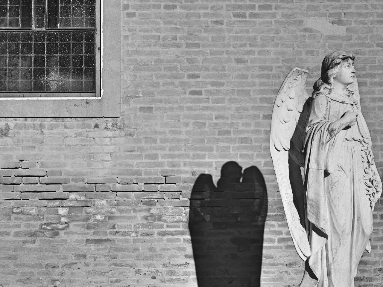 Grayscale Photo of an Angel Near Brick Wall