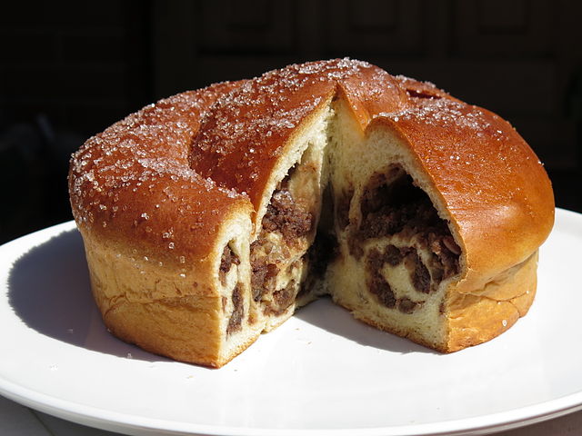 A traditional Italian gubana cake, sliced to reveal its spiral filling of dried fruits and nuts, served on a white plate.