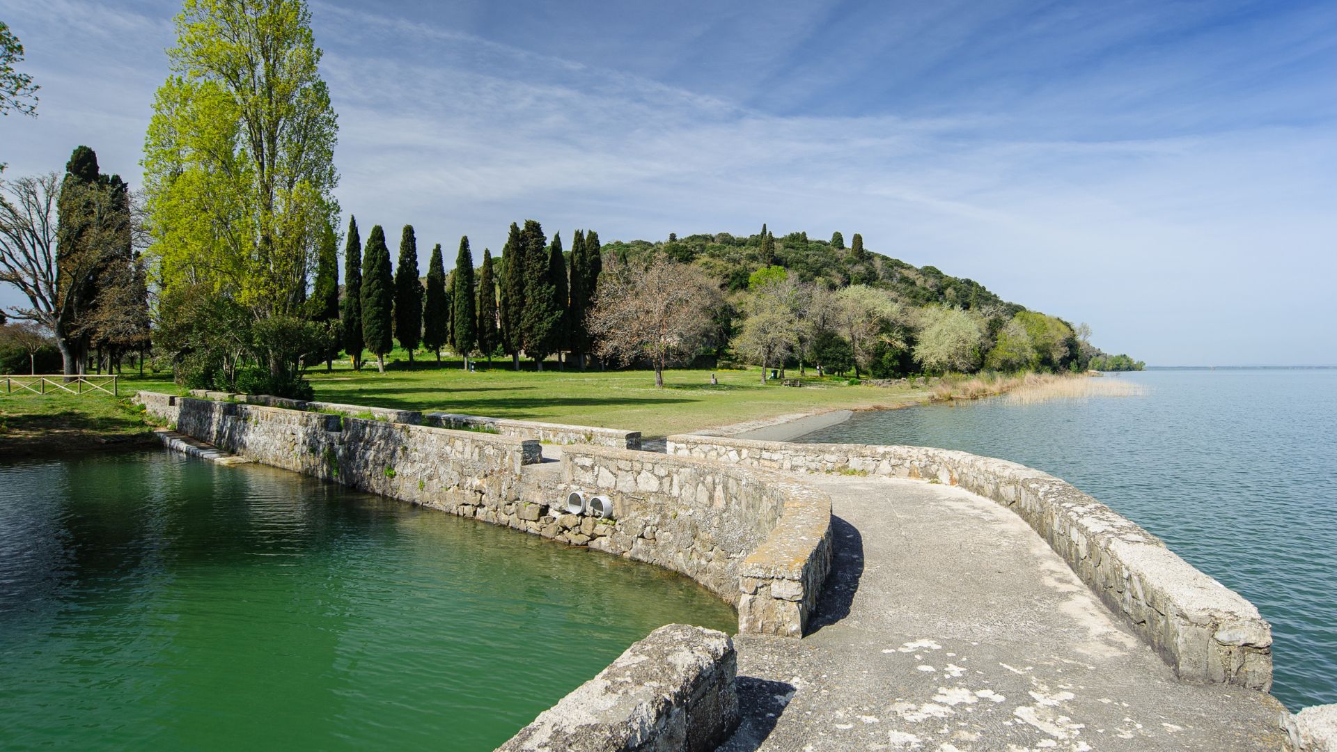 The image shows a stone causeway leading to Isola Polvese on Lake Trasimeno in Umbria, Italy