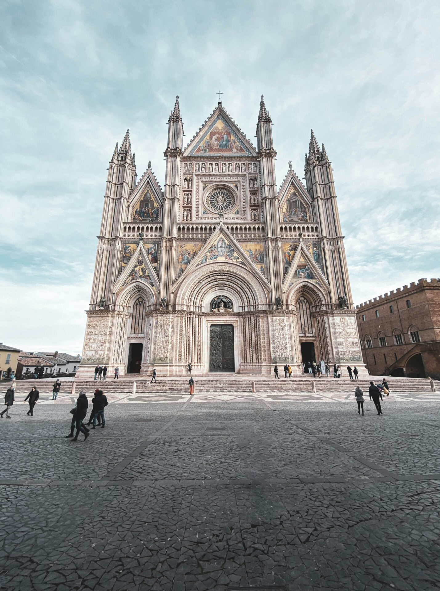 Magnificent façade of the Duomo di Orvieto, adorned with intricate mosaics, rose windows, and Gothic spires under a clear blue sky.