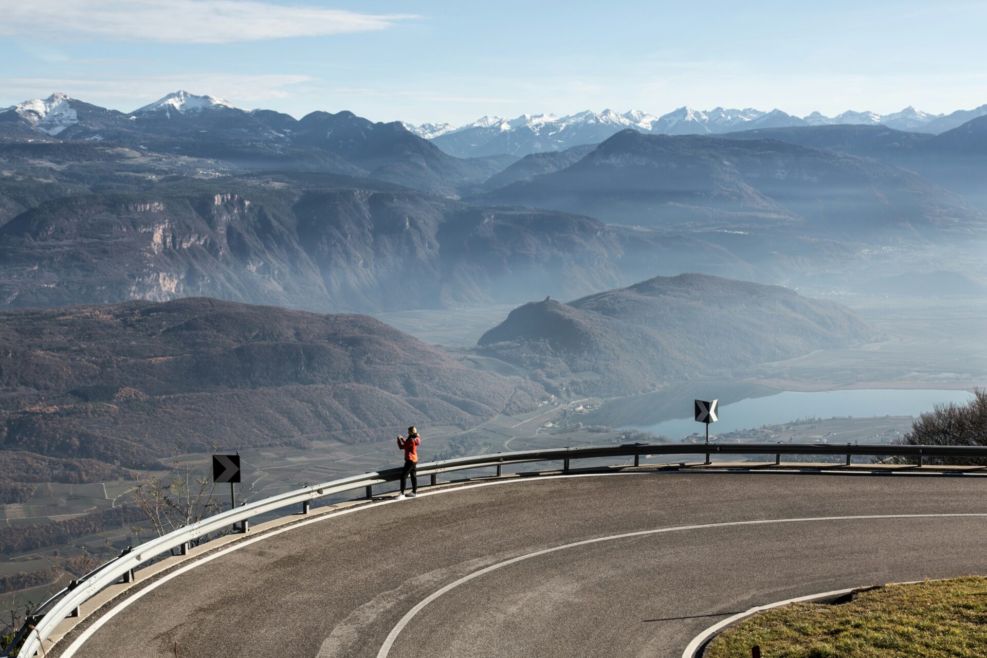 Mendelpass - a person standing at the edge of road on the cliff with mountain landscape behind