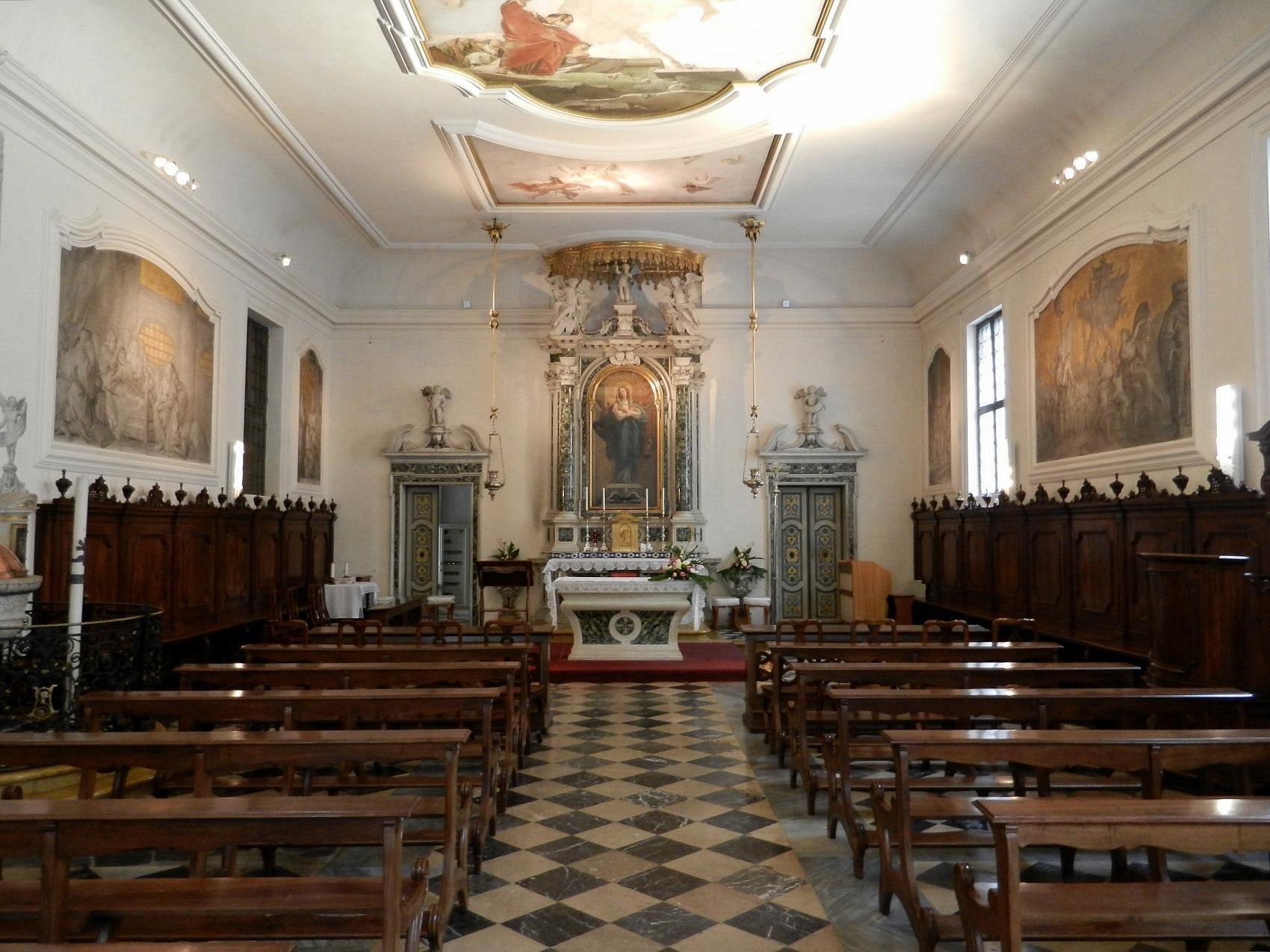 Interior of Oratorio della Purità in Udine, Italy, featuring wooden pews, a detailed altar with religious artwork, painted ceiling panels, and classic frescoes on the walls.