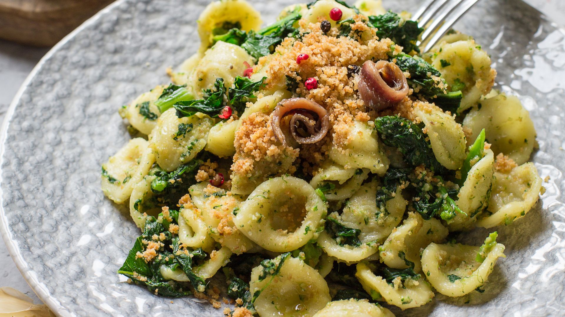 The image shows orecchiette with rapini, a classic dish from the Apulia region of Italy. It consists of "little ears" shaped pasta (orecchiette) tossed with rapini, also known as broccoli rabe. The dish often includes other ingredients such as garlic, olive oil,
