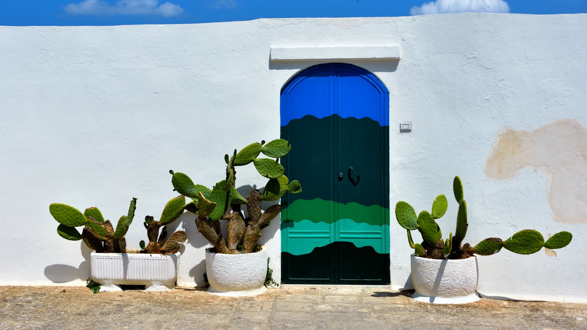 The image shows a street in 'La casa con la porta blu' Ostuni, Puglia, Italy.