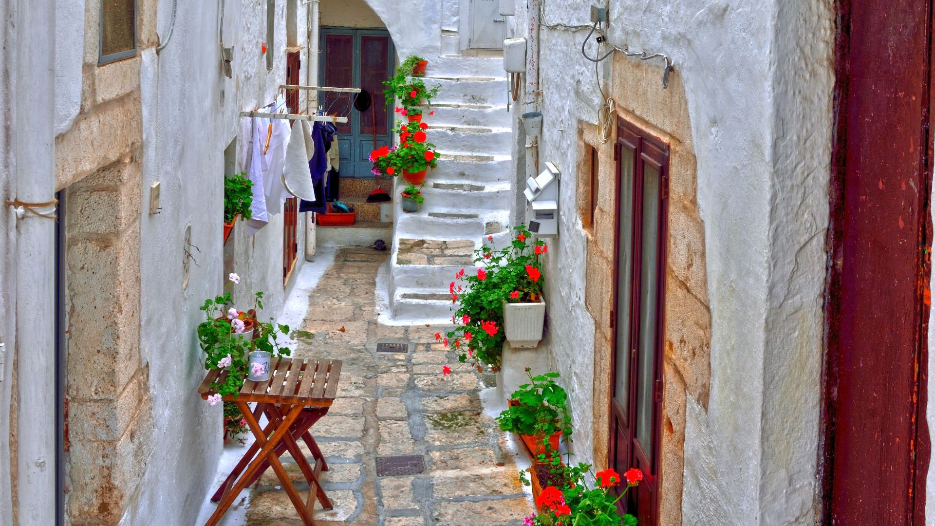 The image shows white houses, with flowers on the side and some clothes hanging in Ostuni, Puglia, Italy.