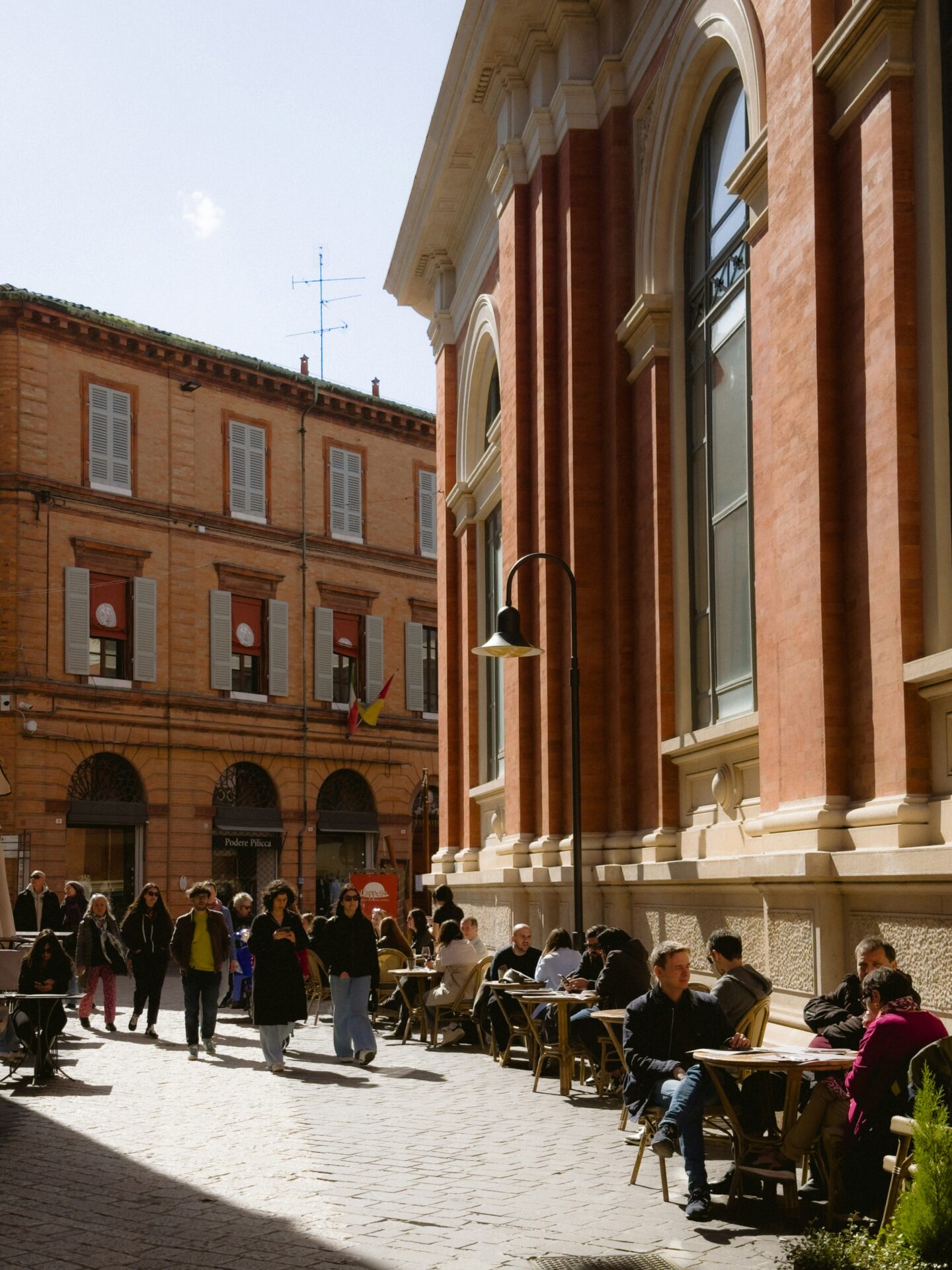 Outdoor café scene in Ravenna with people enjoying coffee and conversation under the sun, surrounded by charming historic buildings.