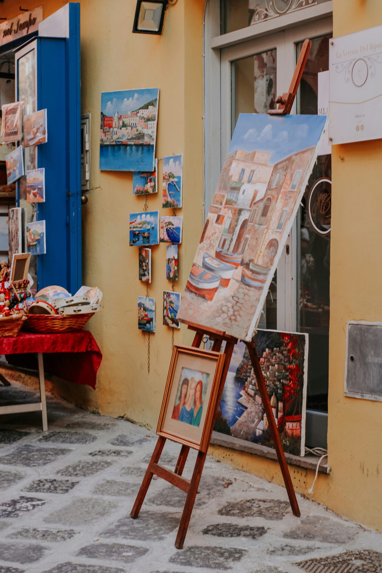 Outdoor painting collection displayed along a narrow street in Procida