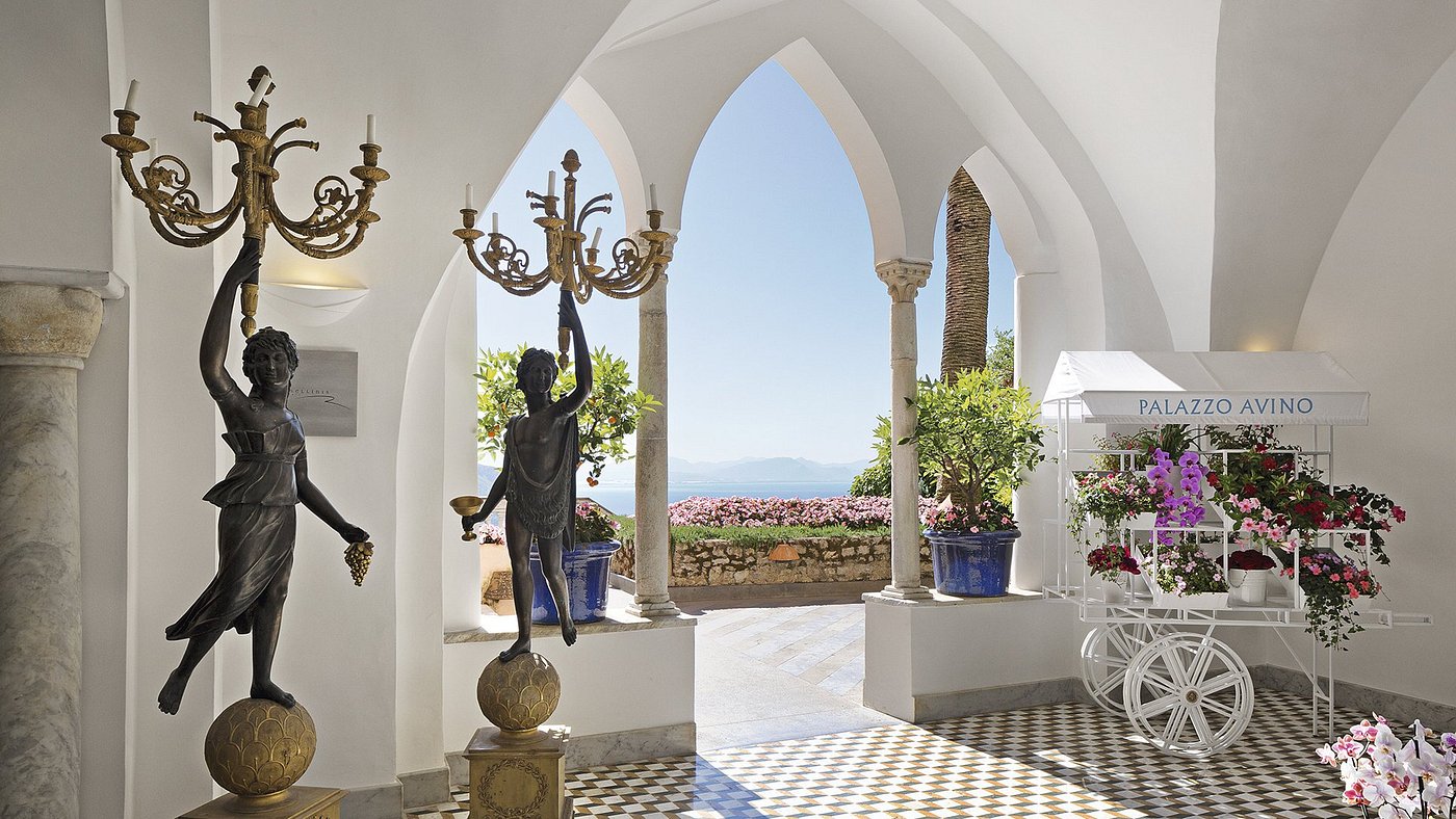 Elegant interior of Palazzo Avino with classical statues, arched windows, floral displays, and a view of the sea in Ravello, Italy.